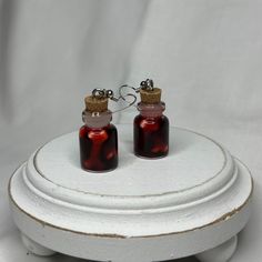 two red glass bottles with cork tops are sitting on a white stand