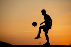 the silhouette of a man playing with a soccer ball at sunset or dawn, on top of a hill