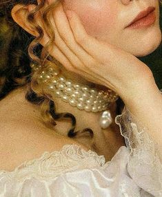 a woman in white dress with pearls on her neck and hands near her face, looking off to the side