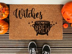 a door mat with the words witches brew on it and two pumpkins in the background