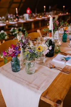 the table is set with many different flowers and candles in vases on each side