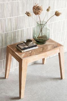 a small wooden table with a glass vase on it and a book sitting on top