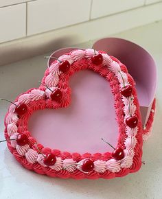 a heart shaped cake sitting on top of a counter next to a box filled with cherries