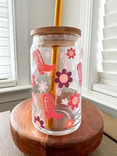 a glass jar sitting on top of a wooden table next to a window with a straw in it