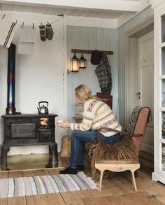 a woman sitting on a chair in front of an open fire place and looking at something