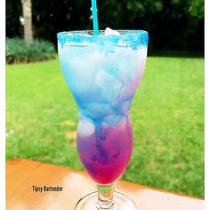 a blue and purple drink sitting on top of a table next to a green field