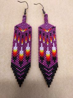 a pair of purple earrings with orange and white designs on them sitting on top of a table