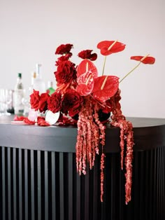 red flowers are sitting on top of a black table with bottles and glasses behind it