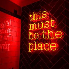 this must be the place neon sign on brick wall with red light in room behind it