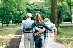 three people are walking down a path in the park, one is holding his arm around the other's back