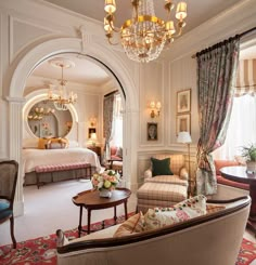 a living room filled with furniture and a chandelier hanging from the ceiling next to a bed