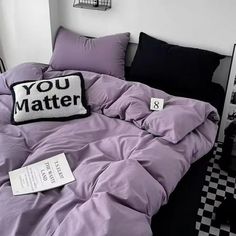 a bed with purple comforter and pillows on it in front of a black and white checkered floor