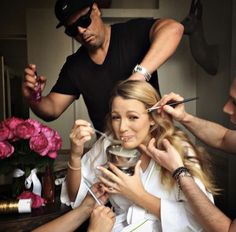 a woman is getting her hair done by two men in front of a table with pink flowers