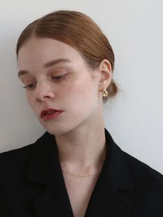 a woman with her eyes closed wearing a black shirt and gold earrings, standing against a white wall