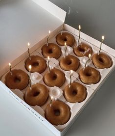 twelve donuts with lit candles in a box