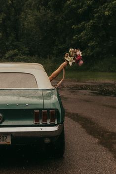 a bride and groom standing in front of a car with their bouquets tied to the hood