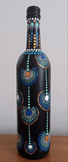 a black vase with blue and orange designs on it sitting on a table next to a white wall