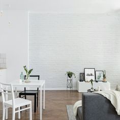 a living room filled with furniture and a white brick wall behind the couch is a dining table