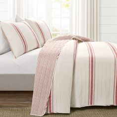 a bed with red and white striped comforter on top of it next to a window