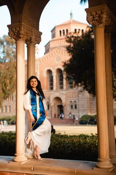 a woman is posing for a photo in front of an old building with columns and arches