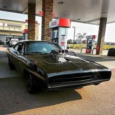 a black muscle car parked in front of a gas station