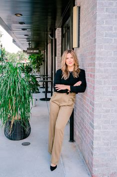 a woman leaning against a brick wall with her arms crossed and looking at the camera