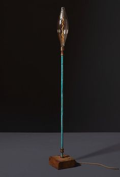 a floor lamp with a wooden base and blue glass shade on the top, in front of a dark background