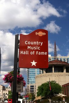 a red sign that says country music hall of fame in front of some tall buildings