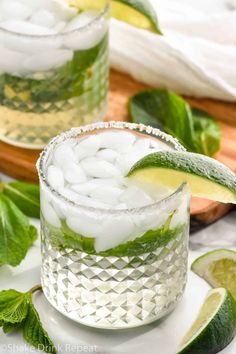 two glasses filled with ice and limes on top of a white plate next to sliced limes