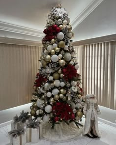 a white christmas tree with red and gold ornaments on it in a living room area