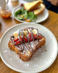 a white plate topped with french toast covered in powdered sugar and sliced strawberries