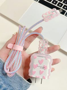 a hand holding a pink and white cell phone charger with hearts on it next to a laptop