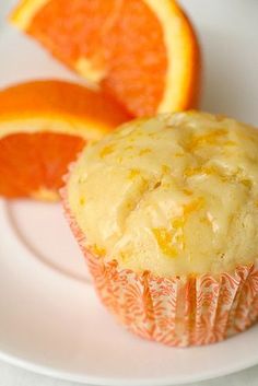 an orange cupcake with frosting on a white plate next to sliced oranges