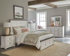 a white bed sitting in a bedroom next to two windows and a rug on top of a wooden floor