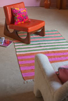 an orange chair sitting on top of a colorful rug next to a white chair with a pink pillow