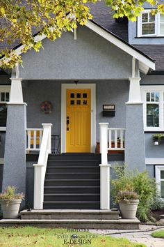 a yellow door is on the front of a gray house with white trim and steps