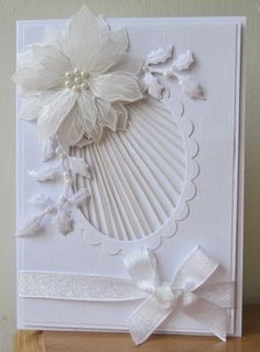 a card with white paper flowers and ribbons on the front, sitting on a wooden table