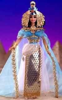 a barbie doll dressed in an egyptian dress and headdress, with pyramids behind her