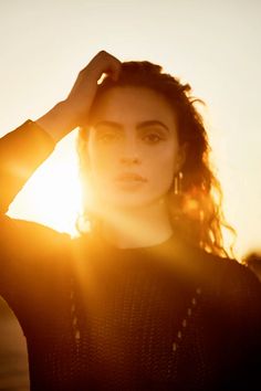 a woman standing in front of the sun with her hands on her head and looking at the camera