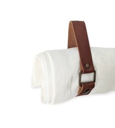 a roll of toilet paper with a brown leather belt on the top and white towel in the bottom