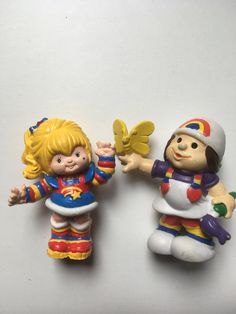 two toy figurines sitting next to each other on a white surface with one holding a butterfly