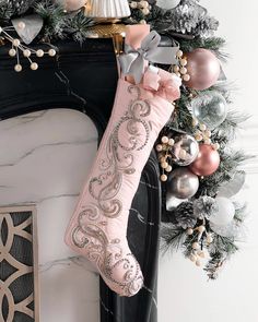 a pink christmas stocking hanging from a fireplace mantel with ornaments and garland around it