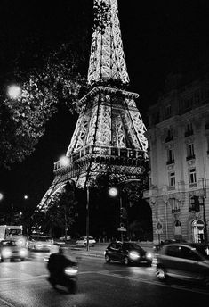 the eiffel tower lit up at night with cars passing by in front of it