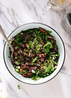 a white bowl filled with green salad on top of a marble counter next to a teapot