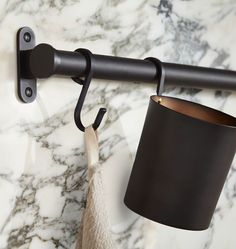 a cup hanging on the wall next to a black curtain rod with a white towel