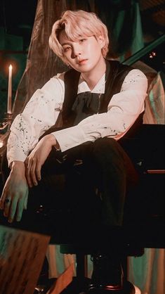 a young man sitting on top of a piano in front of a lit candle and curtain