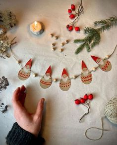 a hand holding a string of christmas decorations on a table with candles and other items