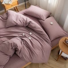 a bed with pink sheets and pillows on top of it next to a wooden table