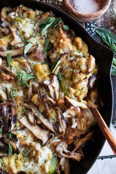 a skillet filled with mushrooms and cheese on top of a table next to utensils