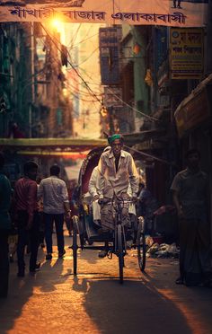 a man riding a bike down the middle of a street with people walking on either side